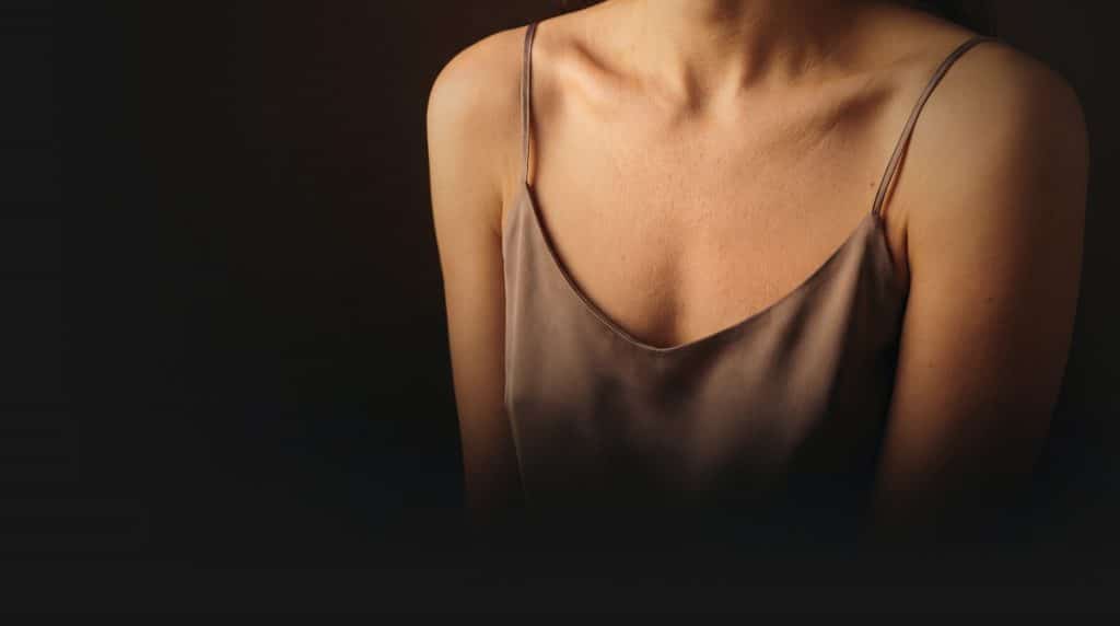 Close-up of a woman's chest and décolletage wearing a silk cami top against a dark background