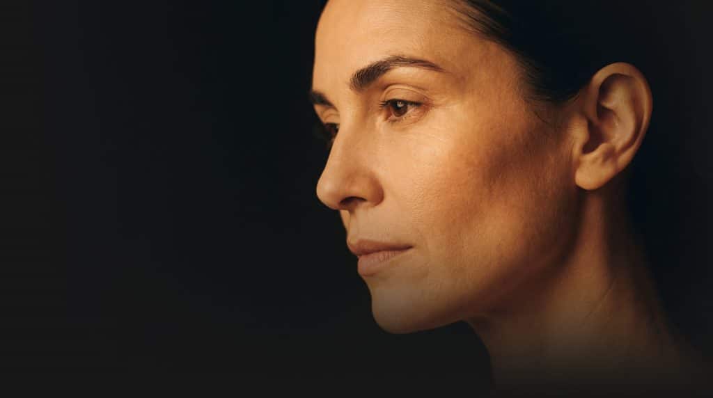 Side profile of a woman's face in warm dramatic lighting against a dark background