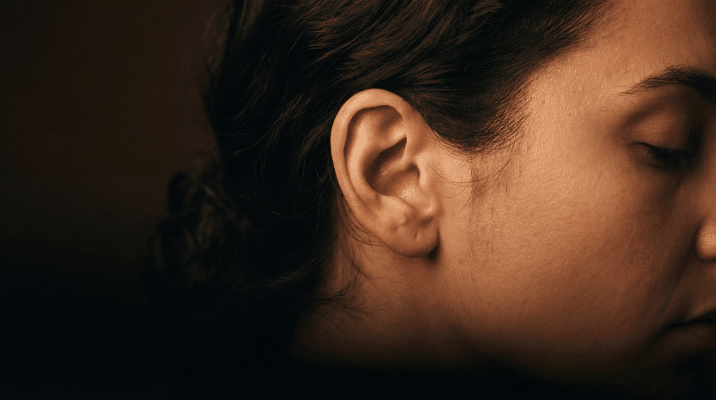 Close-up of a woman's ear and cheek in warm dramatic lighting against a dark background