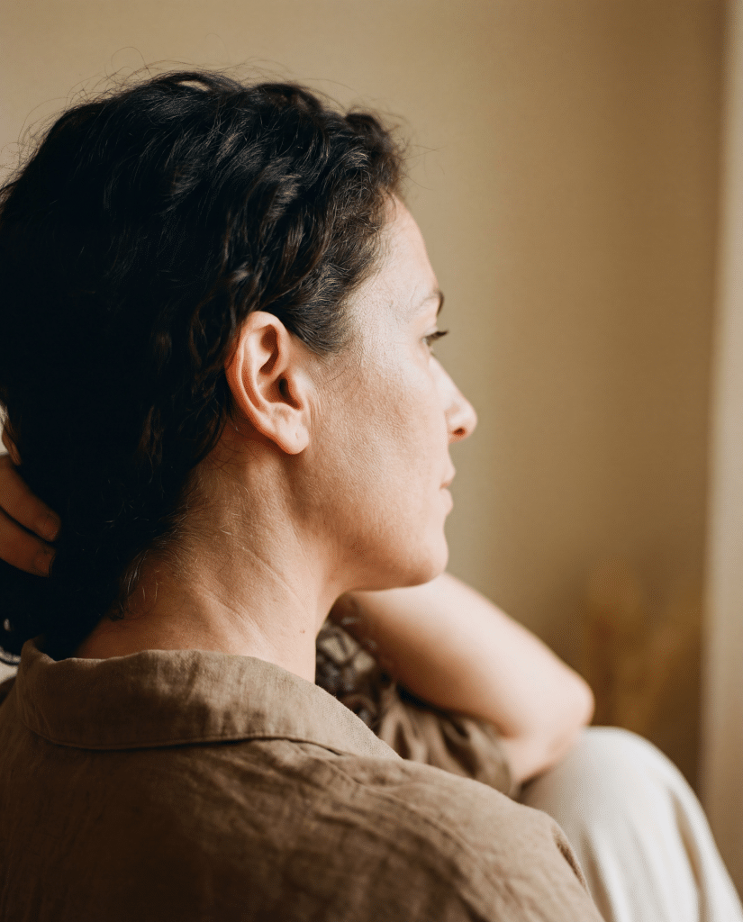 Side profile of a woman with her hair up showing her ear and neck, wearing a linen shirt in soft natural light